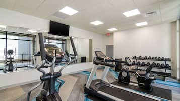 Un gimnasio con cintas de correr, elípticas y un estante con mancuernas.