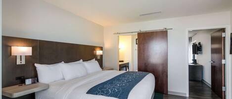 A hotel room with a large bed, bedside tables, a nightstand, a desk, a chair, a TV, and a wardrobe.