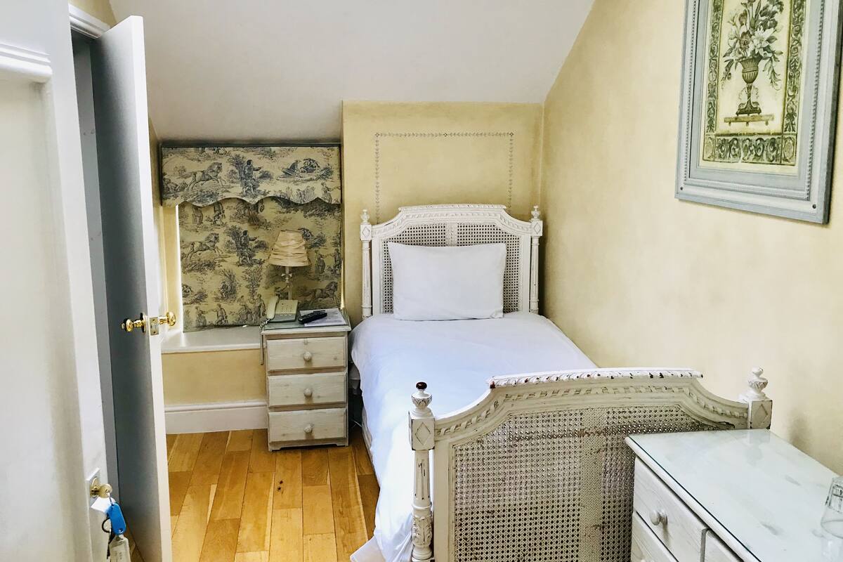 A bedroom with a bed, bedside table, lamp, and a dresser.