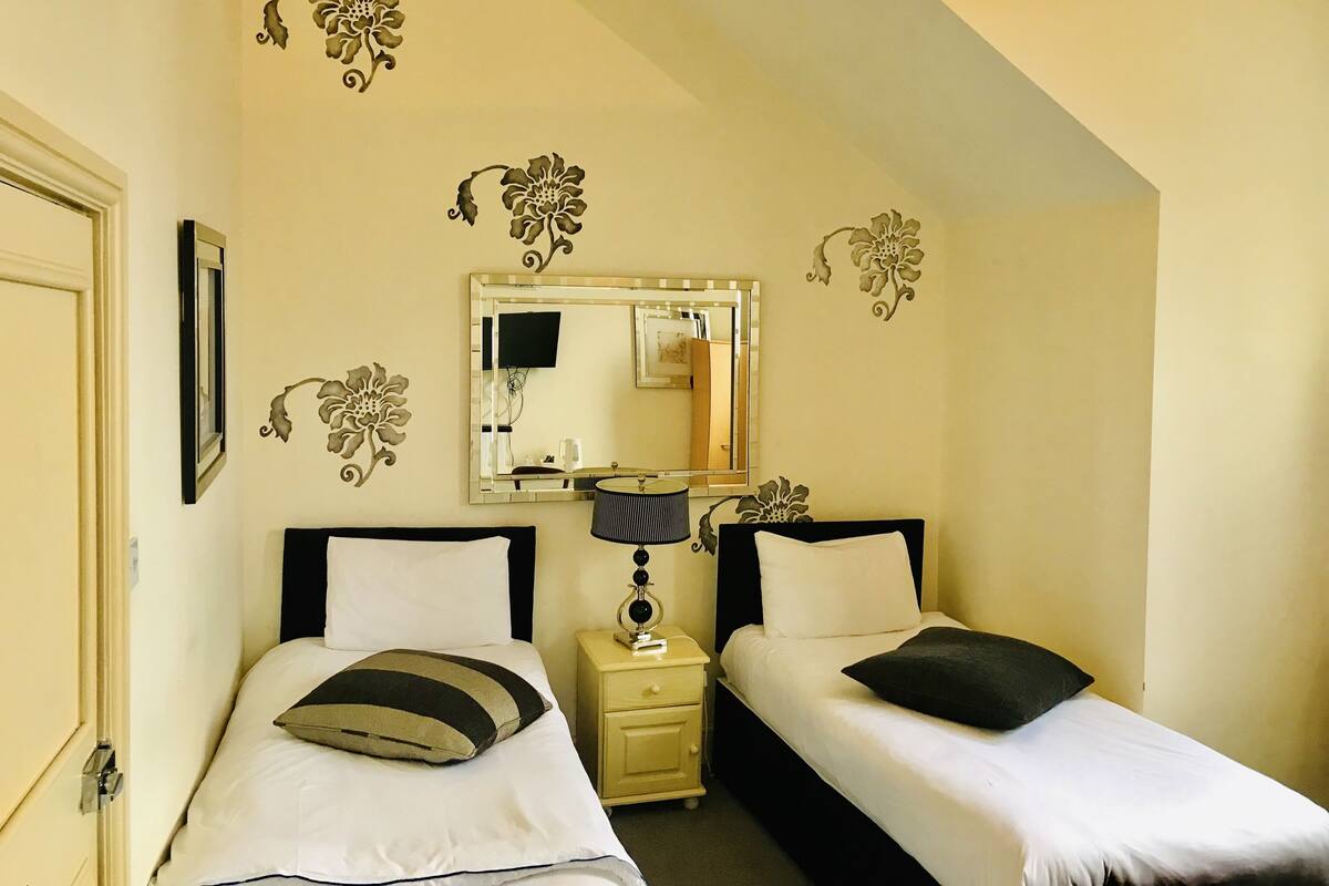 A twin room with two beds, a mirror, a nightstand, and decorative wall stickers.
