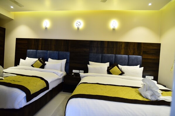 A hotel room with two beds, each with a headboard, white bedding, and a yellow accent. There are wall-mounted lights above the beds and a nightstand with a phone and charger.