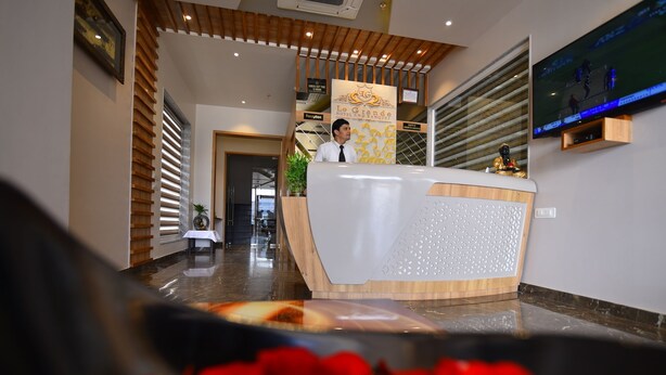 Ein Hotel-Empfangsbereich mit Rezeptionistin, Empfangstresen, einem Fernsehbildschirm und einer Treppe zu einer weiteren Etage.