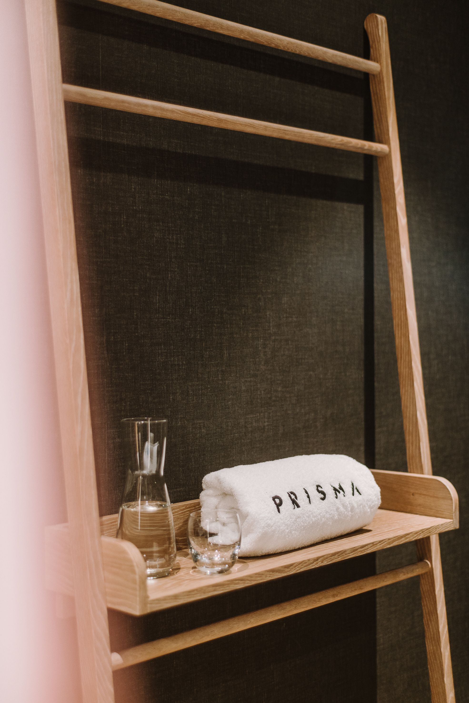 A wooden chair with a towel labeled "PRISMA" and a glass bottle on a shelf.