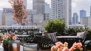 A rooftop terrace with outdoor seating, a view of city buildings, and a tree with pink flowers. - PURO Warszawa Centrum (Warsaw)