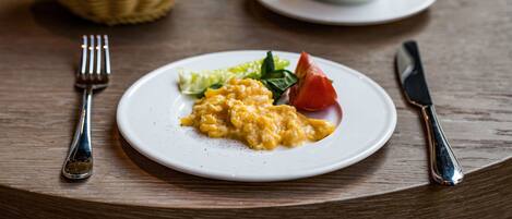Un plato de huevos revueltos, guarnición de vegetales verdes y un tomate, sobre una mesa de madera.