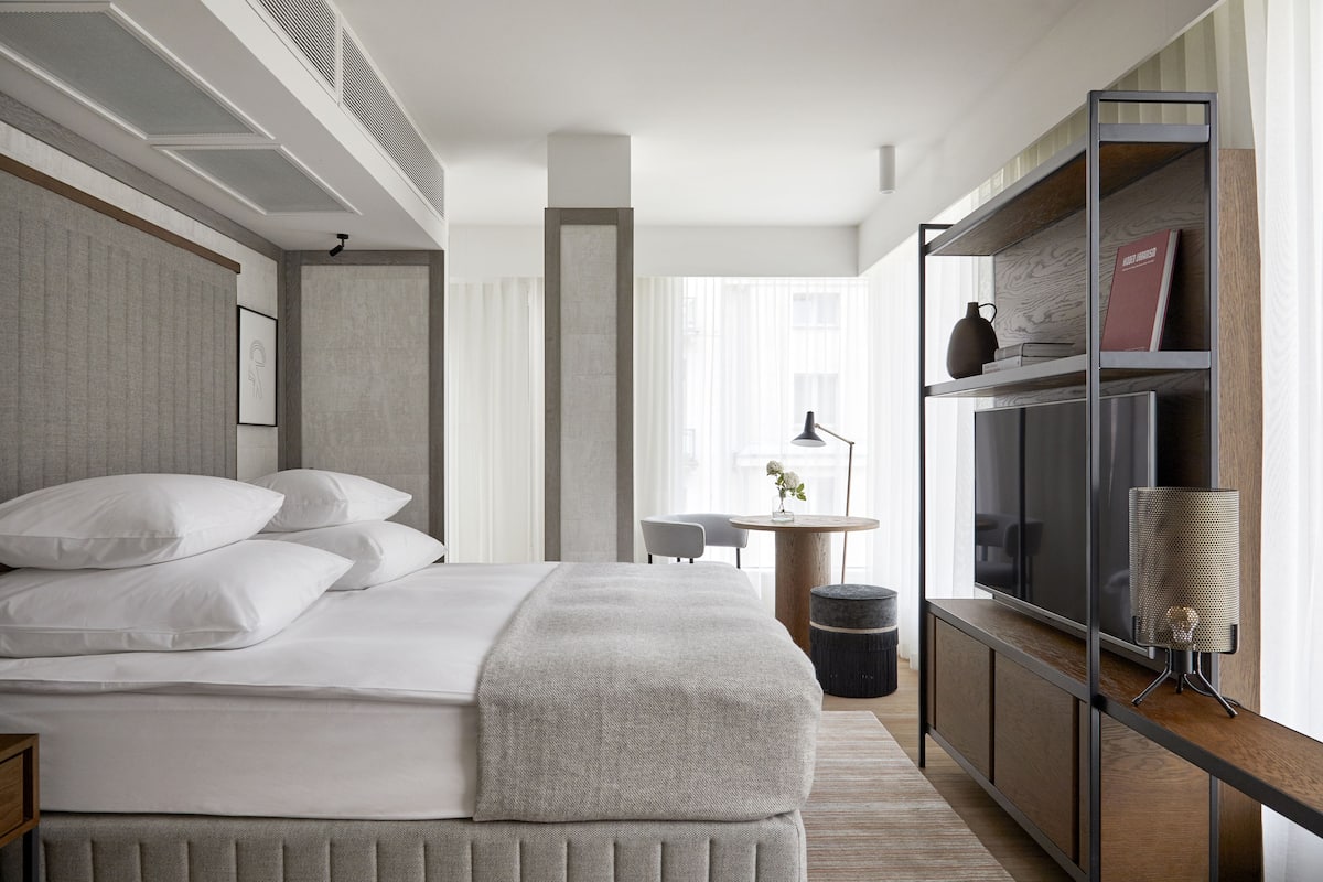 Ein modernes Hotelzimmer mit einem großen Bett, einem Fernseher, einem Bücherregal und einem kleinen Tisch mit einer Lampe.