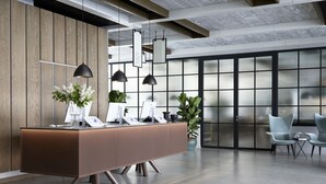 A modern reception desk with a wooden panel backdrop, two pendant lights, and a potted plant. - PURO Warszawa Centrum (Warsaw)