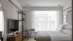 A modern hotel room with a large bed, a TV mounted on a wooden console, a small desk with a chair, and a large window with a city view. - PURO Warszawa Centrum (Warsaw)