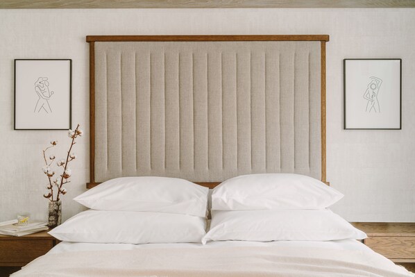 A neatly made bed with a headboard, two framed artworks on the wall, and a bedside table with a vase of dried flowers. - PURO Warszawa Centrum (Warsaw)