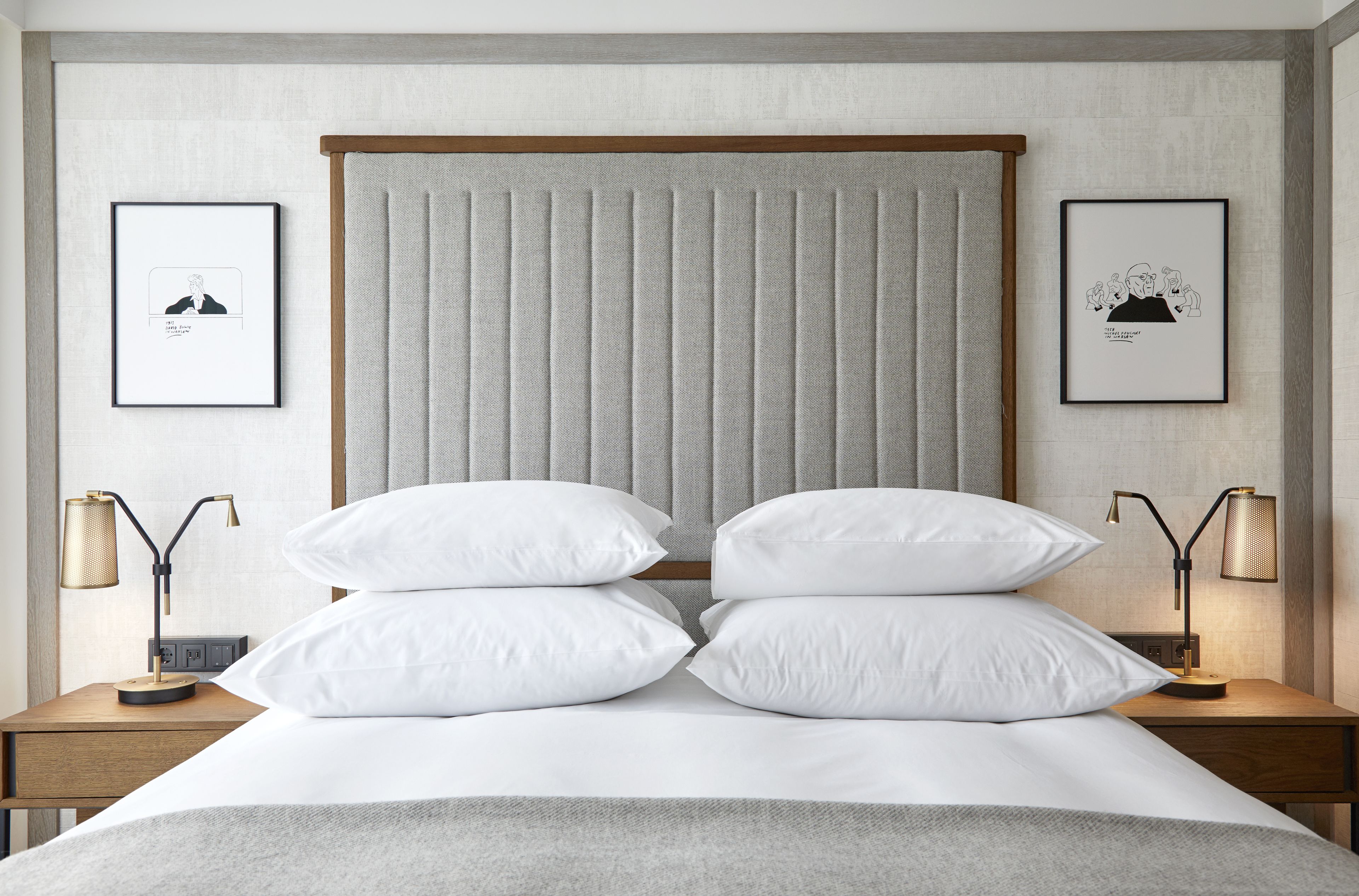 A neatly made bed with white linens, two bedside tables with lamps, and framed artwork on the walls.