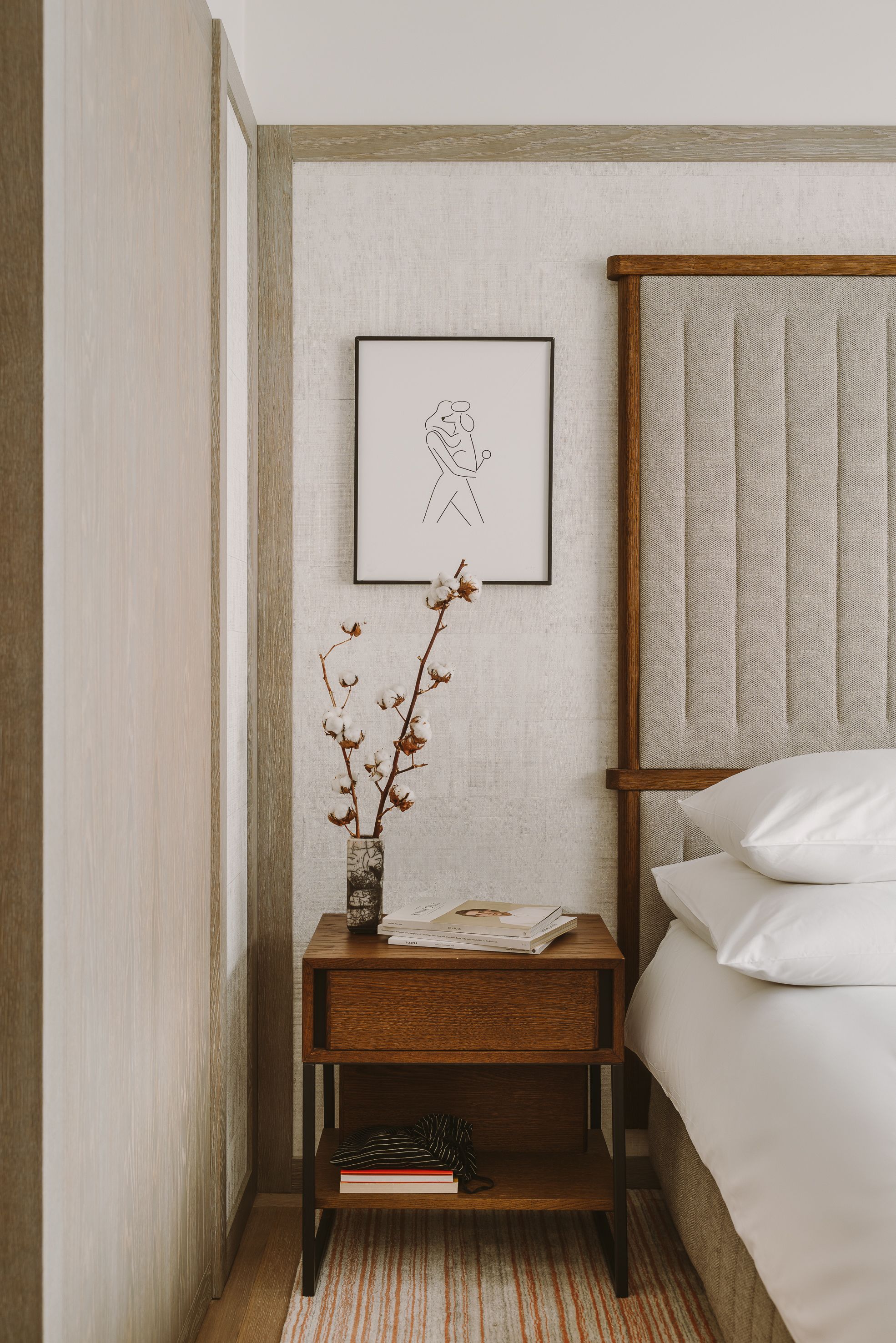 Ein ordentlich eingerichtetes Schlafzimmer mit einem Nachttisch aus Holz, einem gerahmten Bild und einer Vase mit getrockneten Blumen.