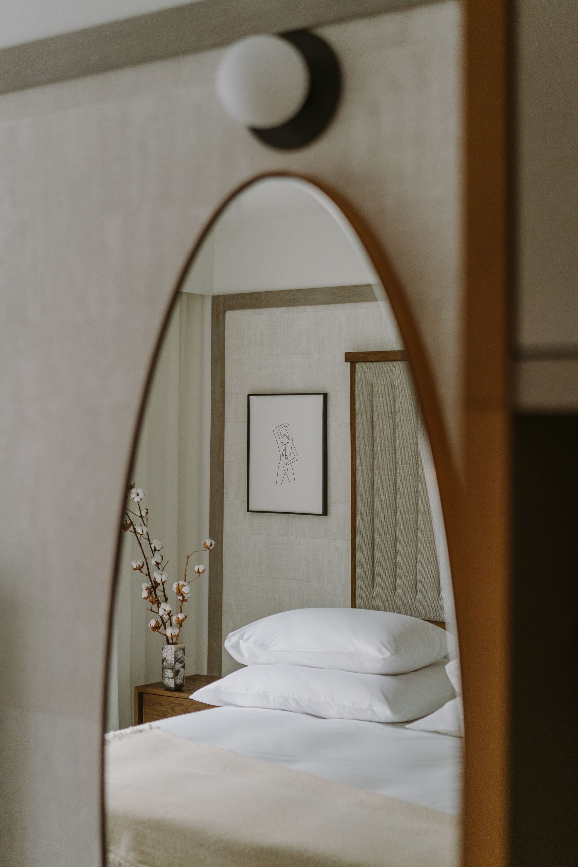 Un dormitorio con cama, mesita de noche, un cuadro en la pared y un florero con flores secas.