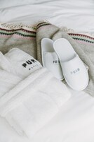 Un par de pantuflas blancas del Hotel Puro y una toalla blanca sobre una cama con una manta estampada.