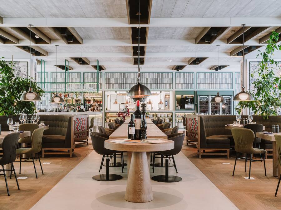 Un restaurante moderno con una mesa redonda central, varias zonas de estar y un bar al fondo.