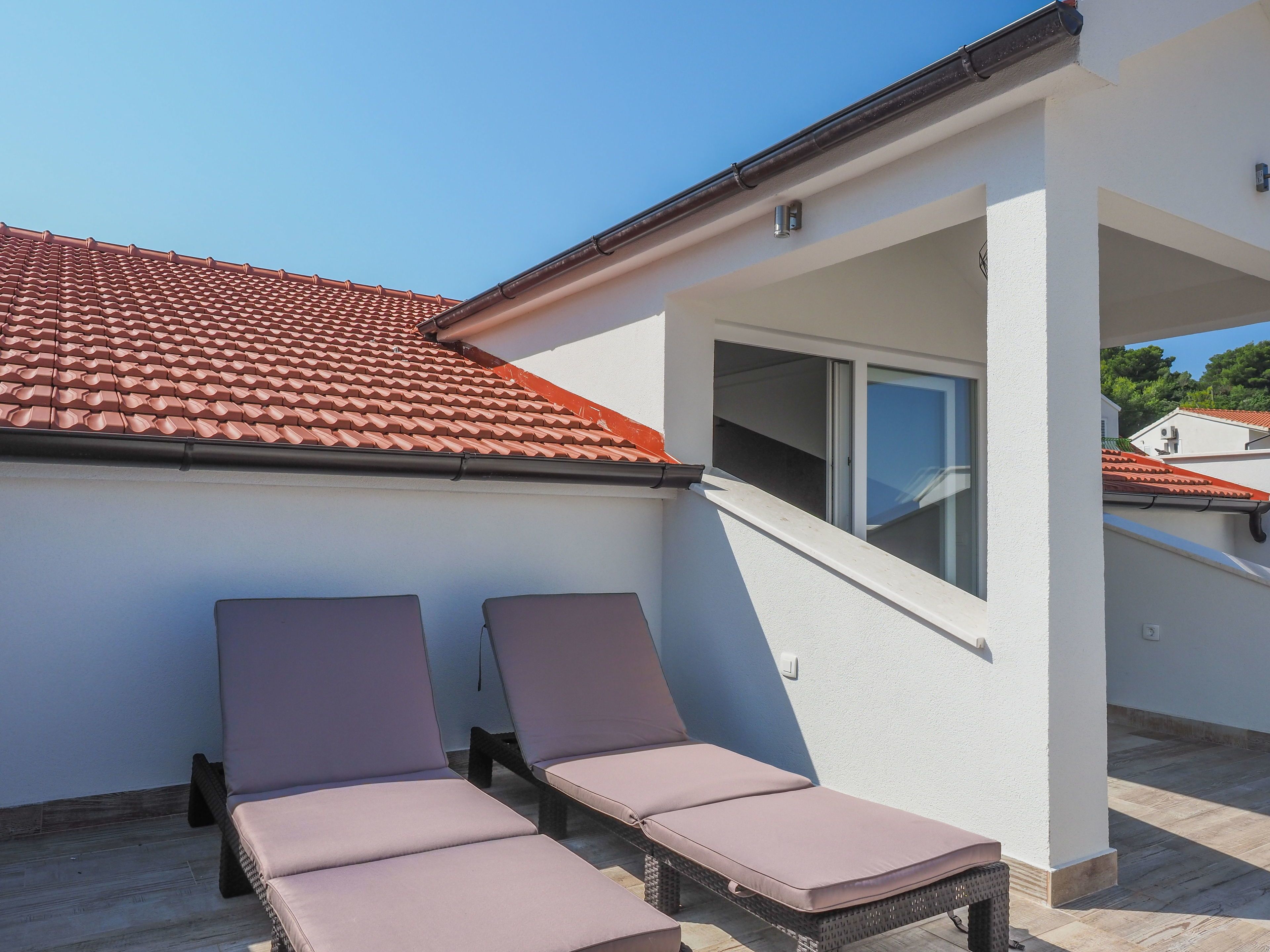 A modern building with a red-tiled roof, two lounge chairs, and a window.