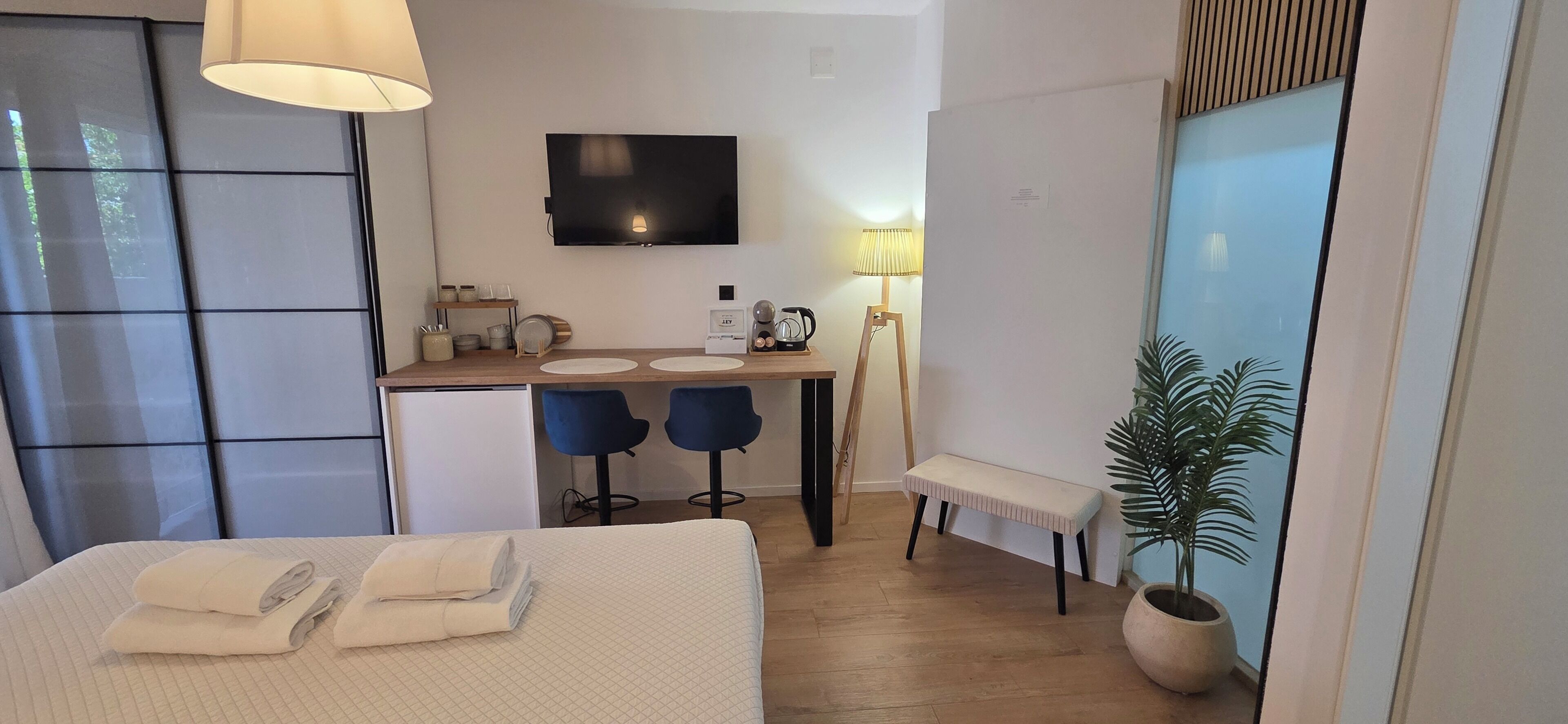 A hotel room with a bed, a desk with two chairs, a television, a lamp, and a potted plant.