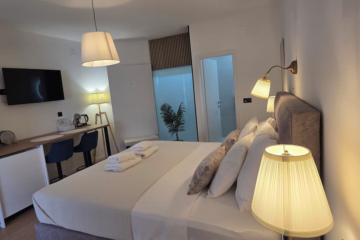 Une chambre d’hôtel comprenant un lit, des lampes de chevet, un bureau avec une chaise, une télévision et une plante.