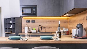 A modern kitchen with a built-in microwave, a wooden countertop, and three grey bar stools. - Apartments Bubalo Hvar (Hvar)