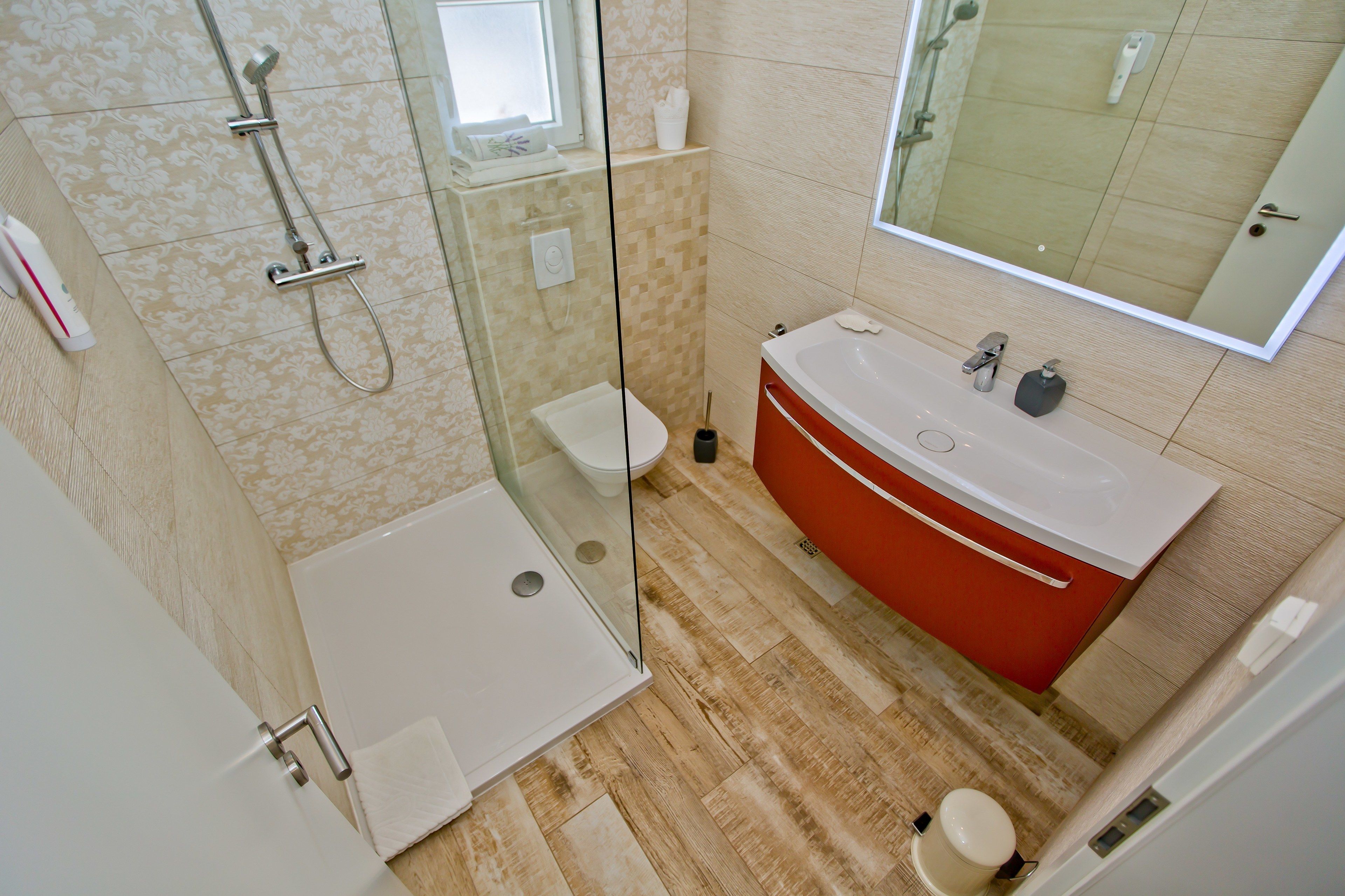 Een moderne badkamer met een douchecabine van glas, een witte badkuip en een rode wastafelmeubel.
