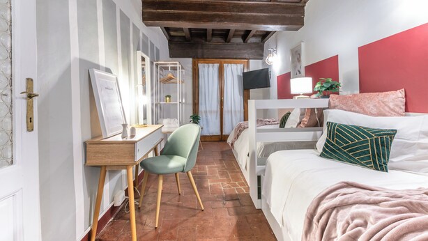 Ein Zimmer mit einem Bett, einem Schreibtisch, einem Sessel, einem Fernseher und einem fenster mit Vorhängen.