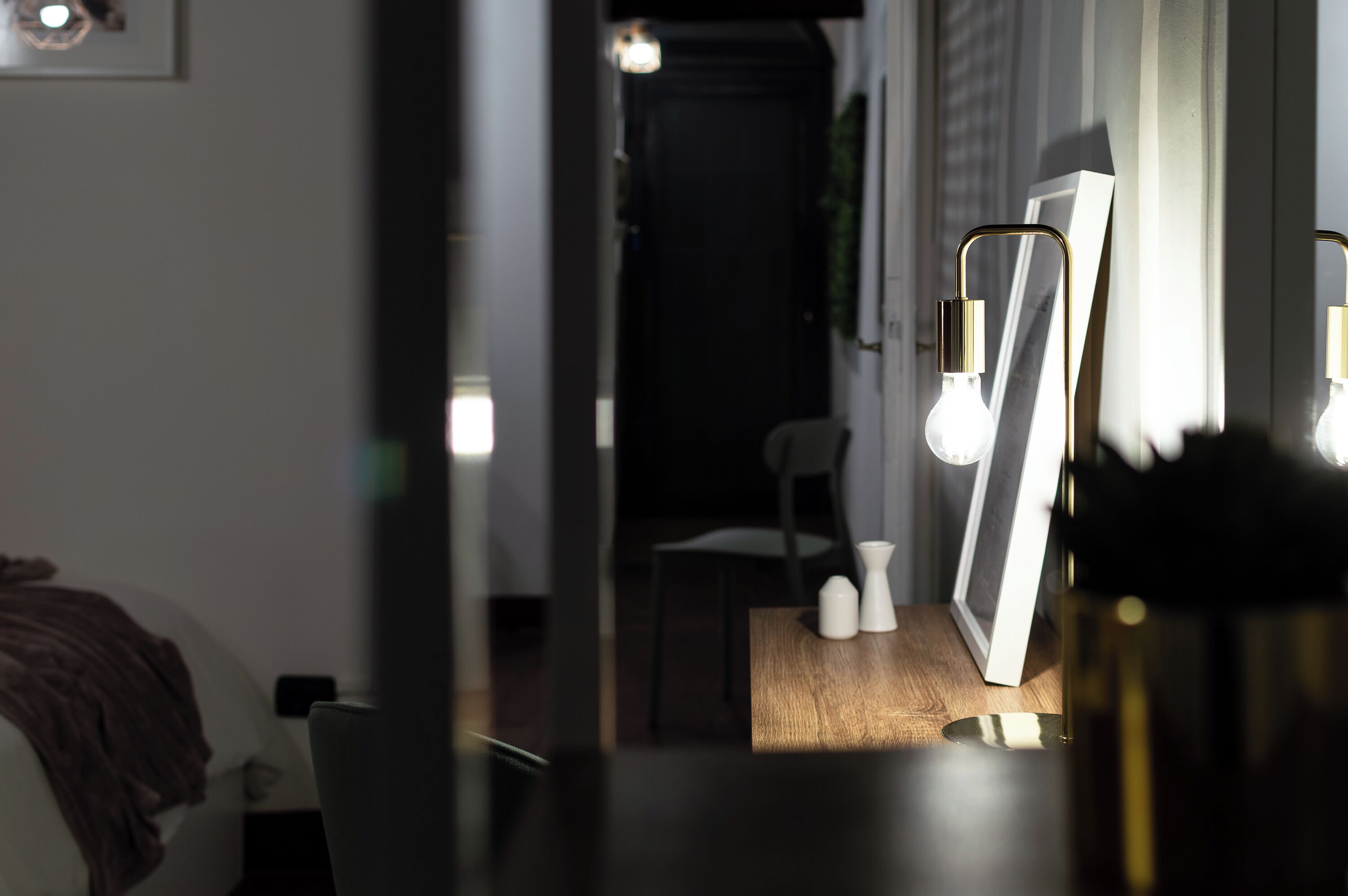 Ein Zimmer mit einem Bett, einem Schreibtisch mit Computer und einem Stuhl. Eine Tür führt in einen weiteren Raum.