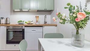 A modern kitchen with green cabinets, a dishwasher, an oven, and a dining table with a vase of flowers.