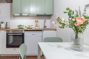 Una cucina moderna con mobili verdi, una lavastoviglie, un forno e un tavolo da pranzo con un vaso di fiori.