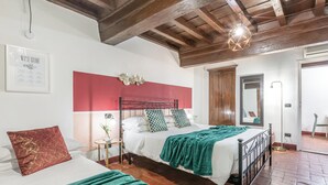 A bedroom with a bed, a side table, a red accent wall, and a wooden ceiling.