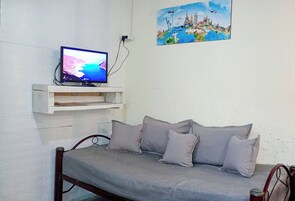 Um quarto com uma cama, uma televisão numa estante e um quadro na parede.