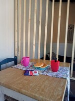 Uma mesa de madeira com toalha de mesa florida, duas chávenas cor-de-rosa, um prato com dois brioches e uma embalagem de snacks.