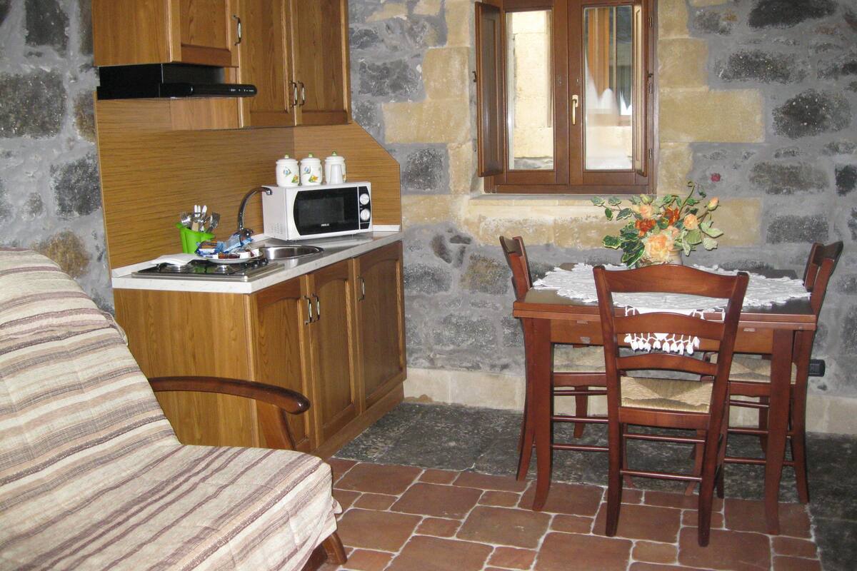 A compact kitchen with wooden cabinets, a microwave, and a dining table with chairs.