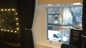 Ein Zimmer mit Fenster, einem grünen Stuhl, einem Schild und einem Spiegel mit Beleuchtung.