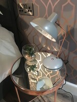 A round glass table with a copper base, a white desk lamp, a glass bowl with a plant, and a power strip.
