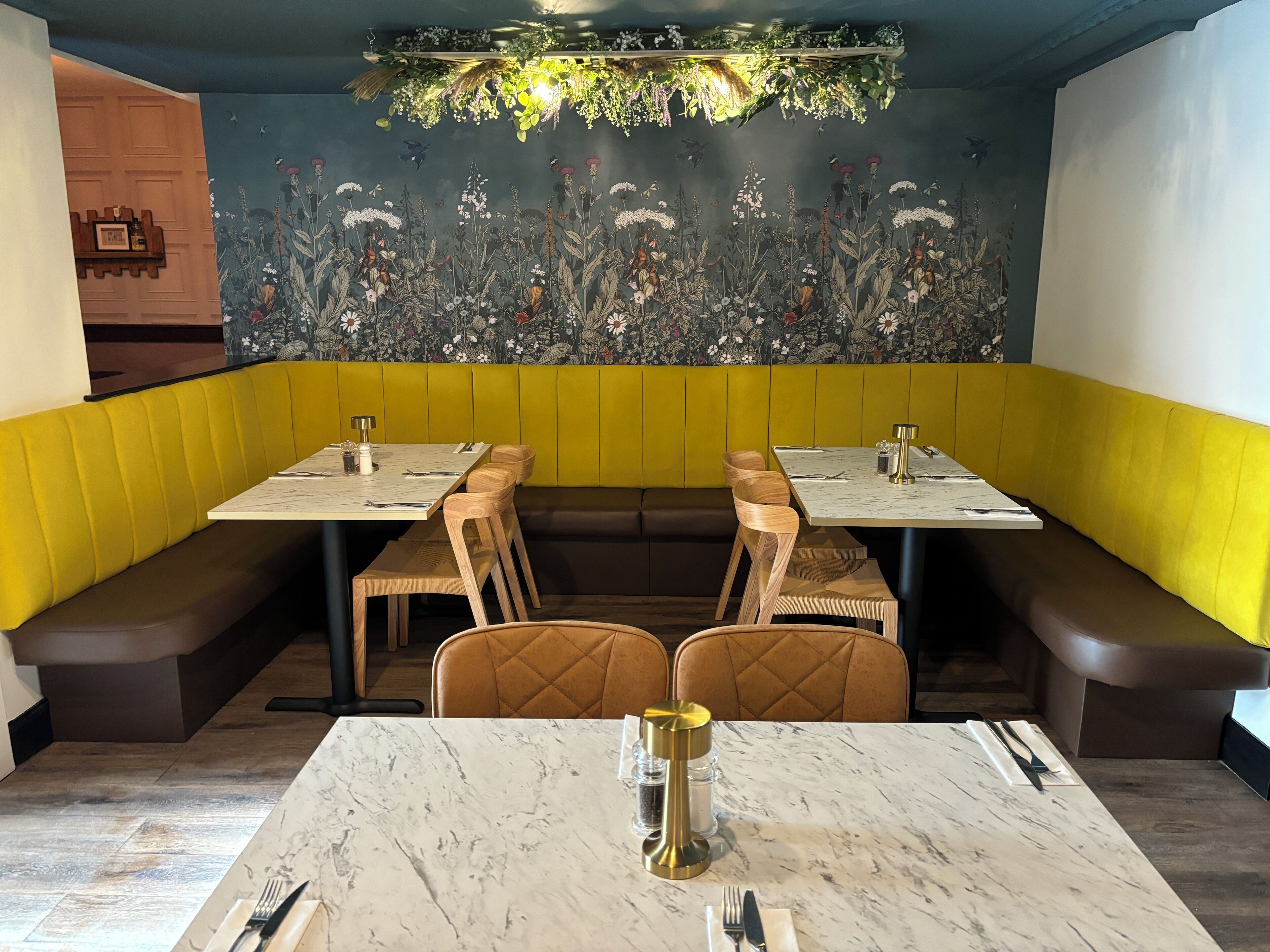Un restaurante con asientos tipo cabina, mesas de mármol y un mural floral en la pared.