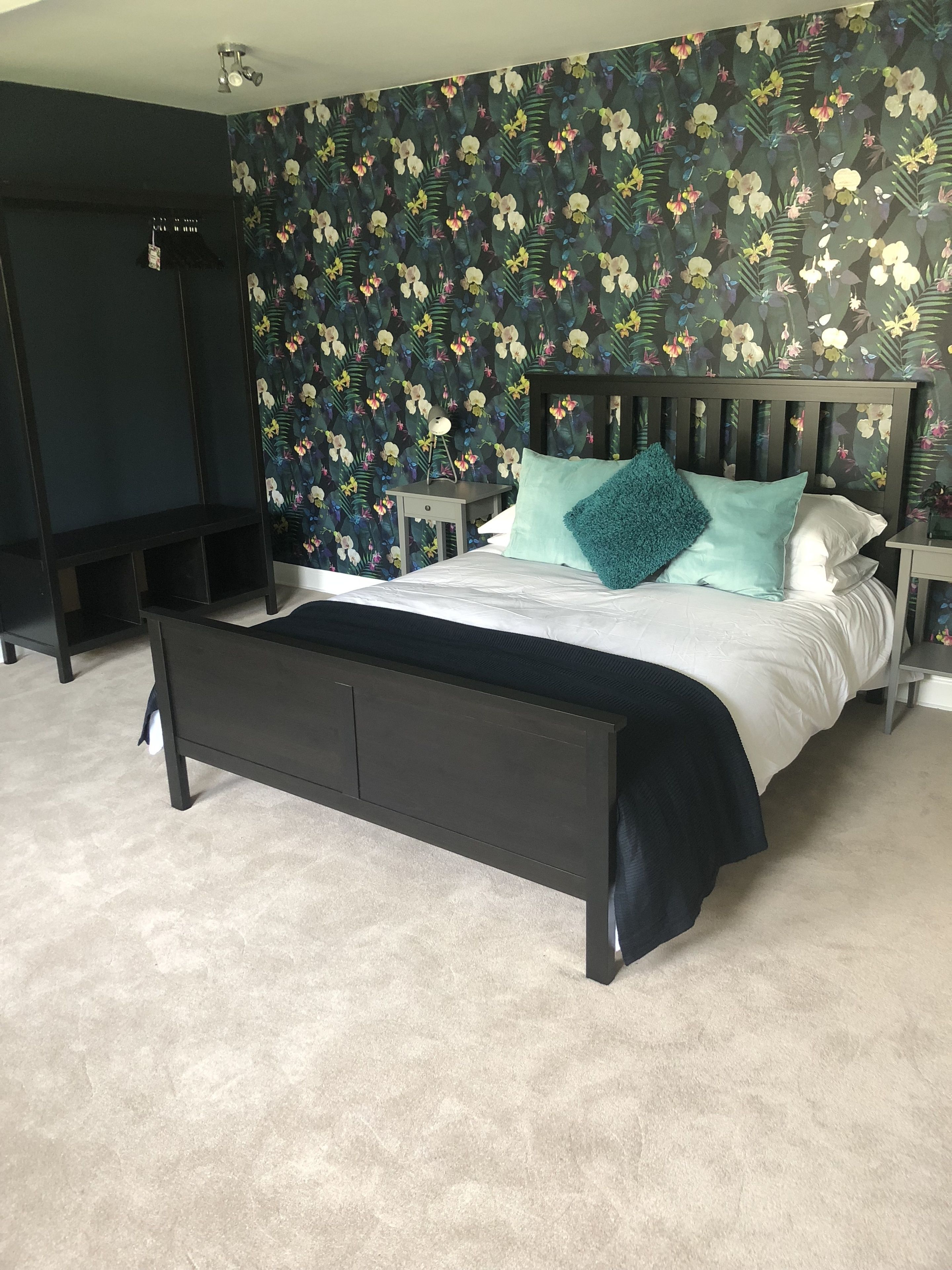 Un dormitorio con una cama, una mesita de noche, un aparador y un papel tapiz floral.