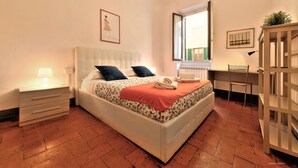 Quarto com cama, mesa de cabeceira, abajur e escrivaninha com cadeira.