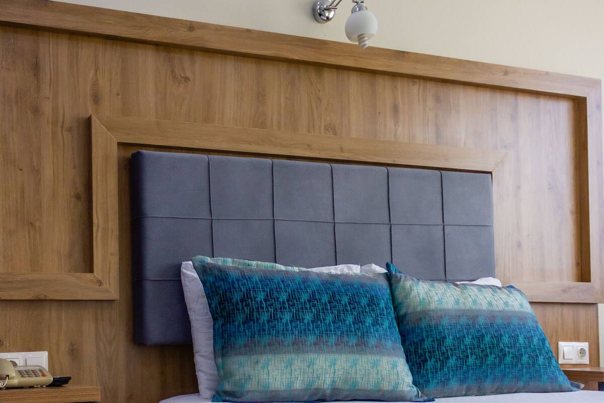 A bedroom with a wooden headboard, a bed with a white and blue blanket, and a nightstand with a telephone.