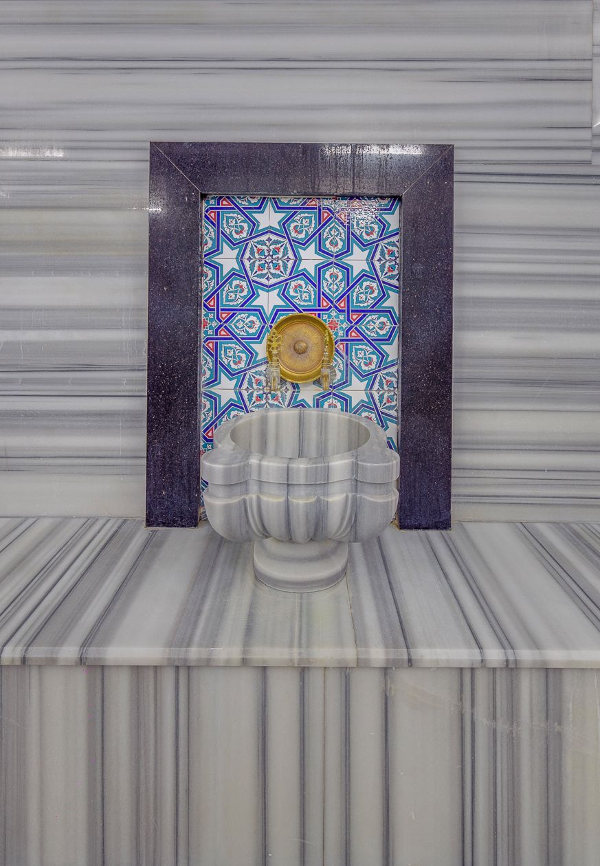 Un bagno con pavimento in marmo, un lavandino ampio e una parete rivestita di piastrelle decorative.