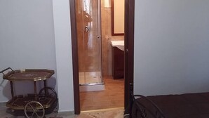 Une pièce avec une porte en bois qui donne sur une salle de bain équipée d’un miroir et d’un lavabo. Un petit chariot à roulettes se trouve à côté de la porte.