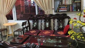 A traditional room with a sofa, a small table, a bookshelf, and a window with curtains. - MaiLy Hostel (Hue)