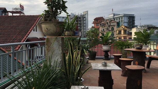 A rooftop terrace with potted plants, outdoor seating, and a view of surrounding buildings. - MaiLy Hostel (Hue)