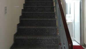 A staircase with a handrail, leading to a room with a white wall and a red carpet. - MaiLy Hostel (Hue)