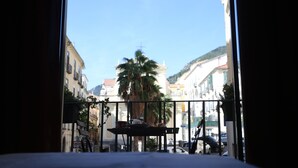 Un balcón con una mesa y sillas, con vista a una calle con edificios y una palmera.