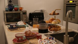 Una encimera de cocina con cafetera, tostadora, microondas y una variedad de bollería y productos para el desayuno.