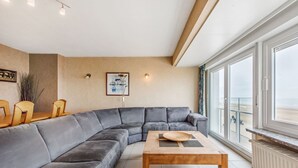 A modern living room with a grey sectional sofa, a wooden coffee table, and a large window offering a view of the sea. - Cortina 201 (Koksijde)
