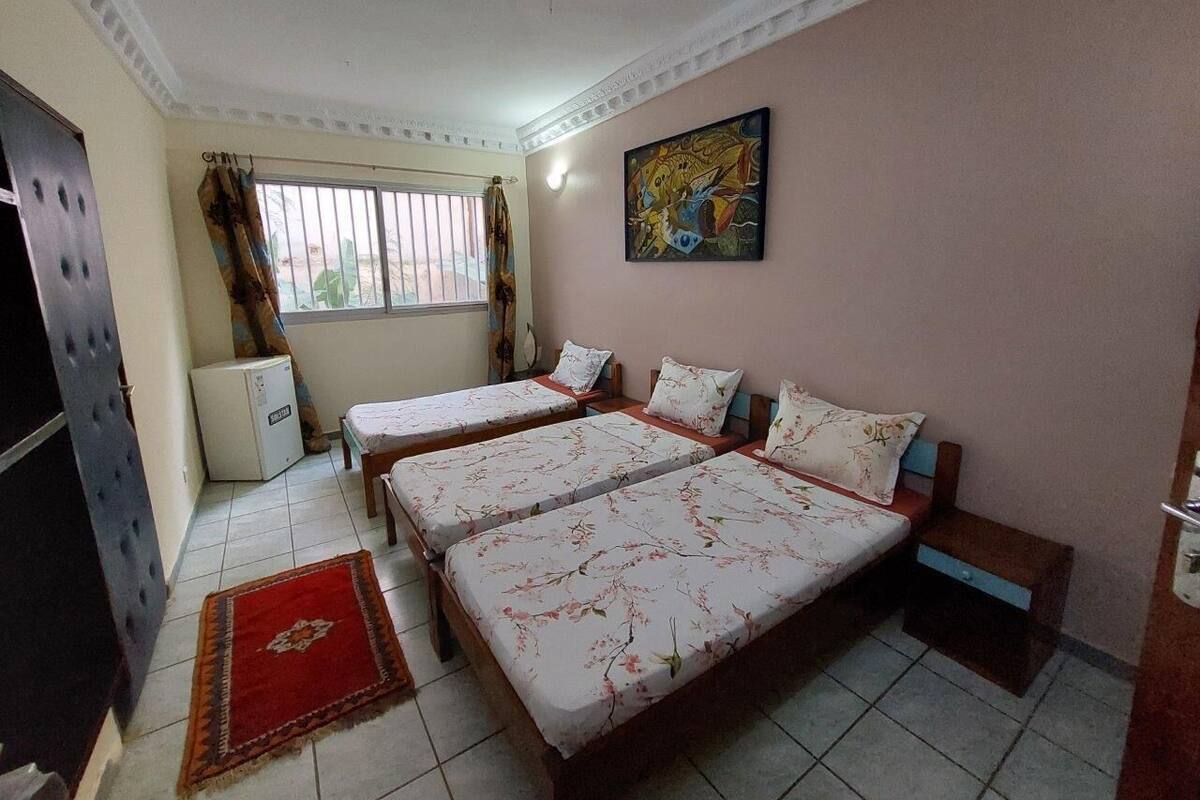 A hotel room with two beds, a small refrigerator, a window with curtains, and a painting on the wall.