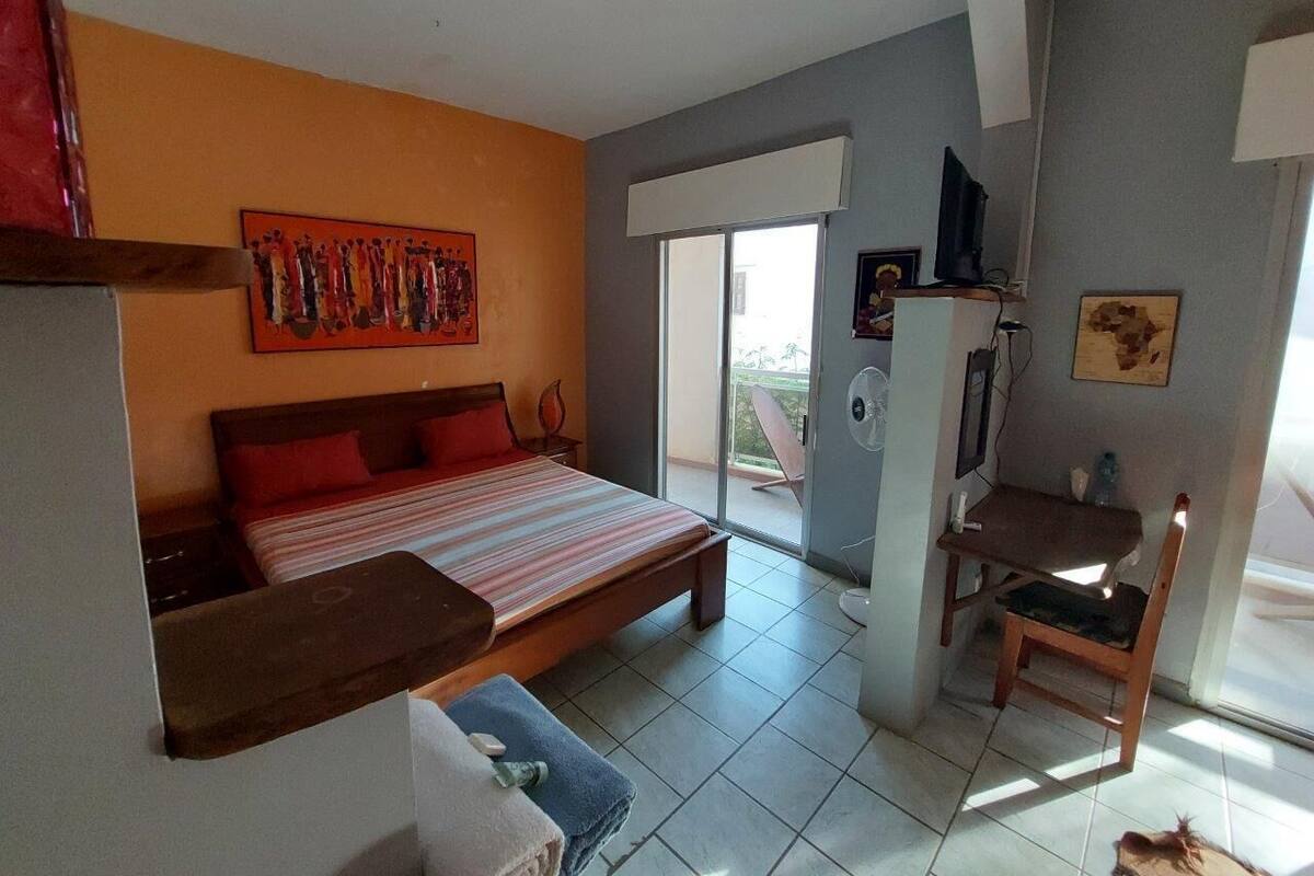 A bedroom with a bed, a desk, and a chair. There is a window and a door.