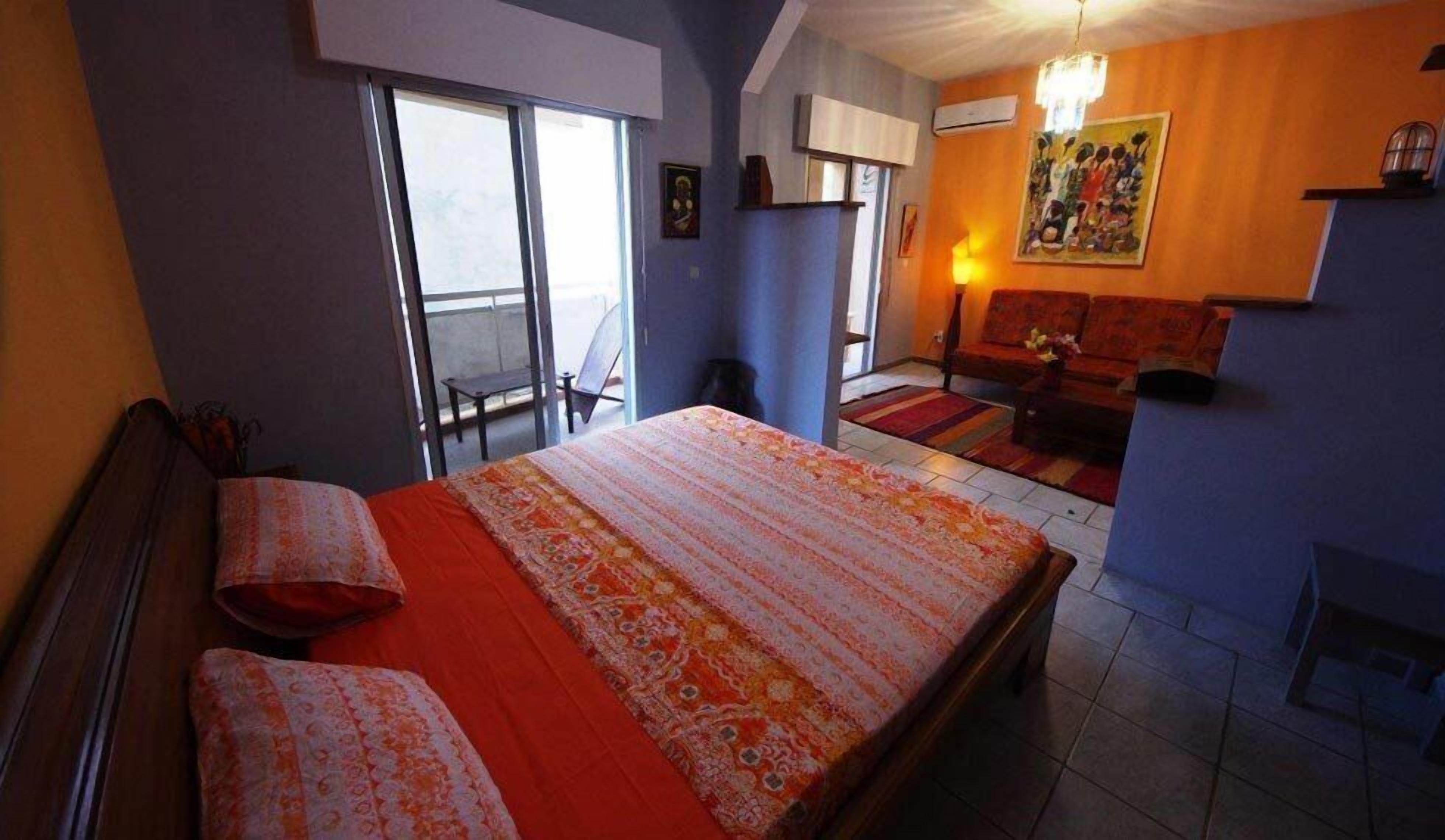 A bedroom with a large bed, a sofa, and a dining table. There is a balcony with a chair and a table.