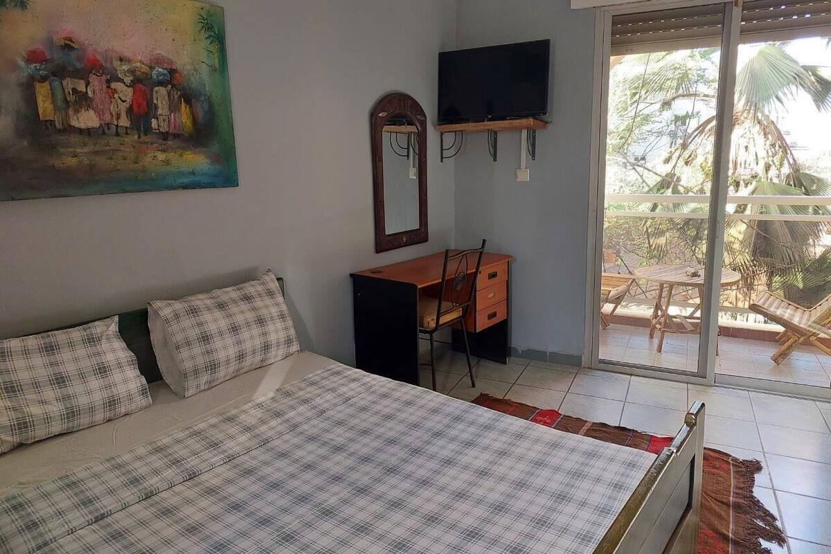 A bedroom with a bed, a desk, a television, and a balcony with outdoor furniture.