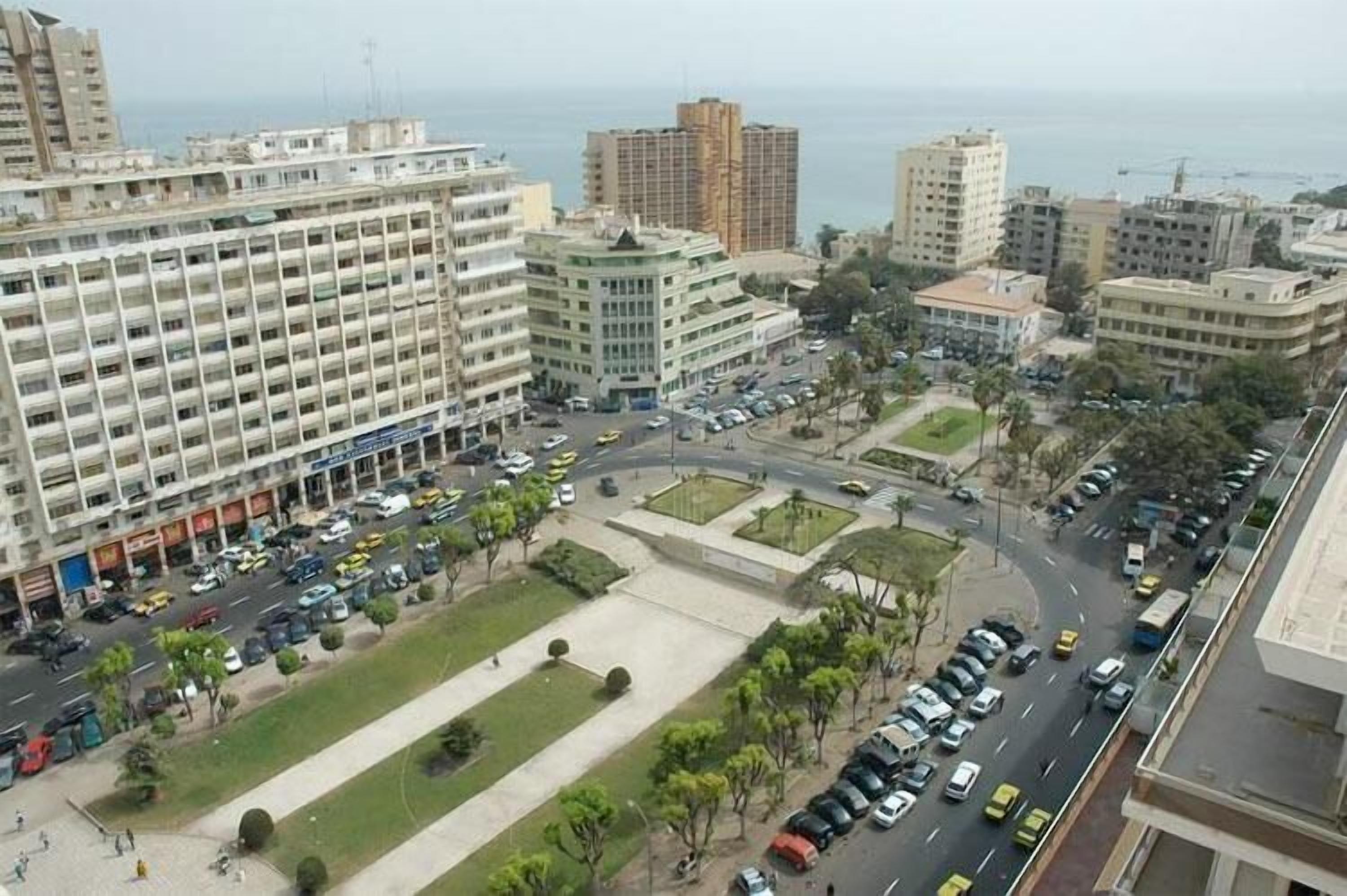 A high-rise building with multiple floors, a parking lot, and a road with vehicles.